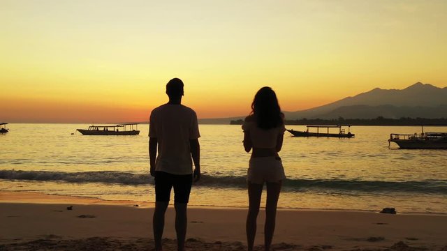rear view of couple silhouette admiring sunset at tropical sea. boats floating in the water. enjoying honeymoon romantic traveling vacation, summer holiday tropical islands
