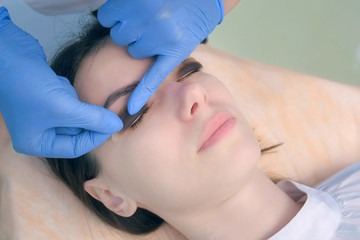 Lift eyelash procedure in beauty salon for young woman, face closeup. Beautician applying curler on eyelid, hands in gloves closeup. Lash lamination in cosmetology clinic.