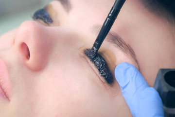 Beautician applying paint on lashes using brush, lift eyelashes procedurein beauty salon, woman...