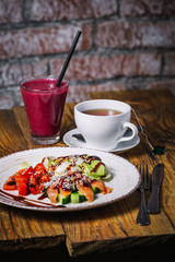 Plate of salmon salad, glass of berry smoothies and cup of tea on wood bakground