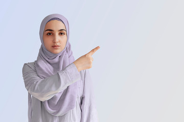 Cute Muslim woman with cheerful face expression points away with her forefinger, showing to copy space on the corner. Portrait of Muslim prayer woman in hijab