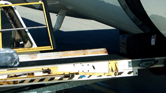 Unloading the luggage from the fuselage of aircraft. The baggage ride on the conveyor when unloading the air plane on the airport.