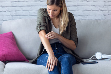 Obraz premium Uncomfortable young woman scratching her arm while sitting on the sofa at home.