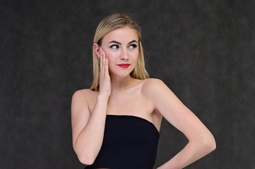 Fototapeta na wymiar The concept of fashionable glamor, cosmetics and beauty with a pretty girl. Portrait of a fashionable beautiful blonde model with long hair, great makeup, on a gray background.