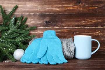 Obraz na płótnie Canvas Knitted mittens with fir tree branches and cup on brown wooden background
