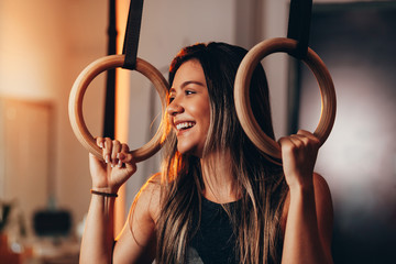 Exercising woman holding gymnast rings. Female taking rest after intense dip ring workout at gym.