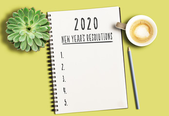 top view of notepad with text 2020 New Years Resolutions and numbered list on yellow desk with...