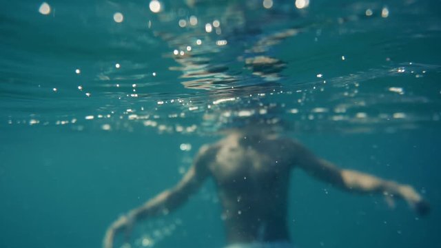 Swimming Man On Blue Sea Underwater.Underwater Man Swimming In Slow Motion With Air Bubbles.Air Bubbles In Water.Water Drops Falling And Splashing On Glassy Water Surface Blue Ocean.