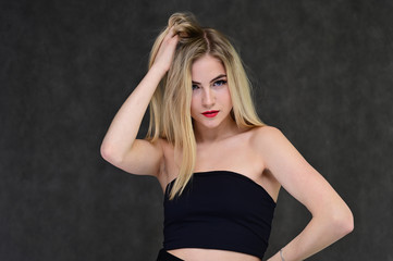 Fototapeta premium The concept of fashionable glamor, cosmetics and beauty with a pretty girl. Portrait of a fashionable beautiful blonde model with long hair, great makeup, on a gray background.
