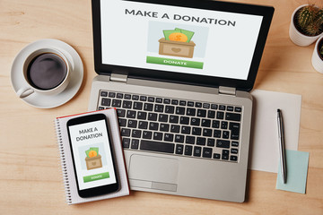 Donation concept on laptop and smartphone screen over wooden table. Top view