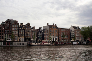 View of Amstel river, canal boat houses and historical, traditional and typical buildings reflecting Dutch architectural style in Amsterdam. It is a summer day with cloudy sky.