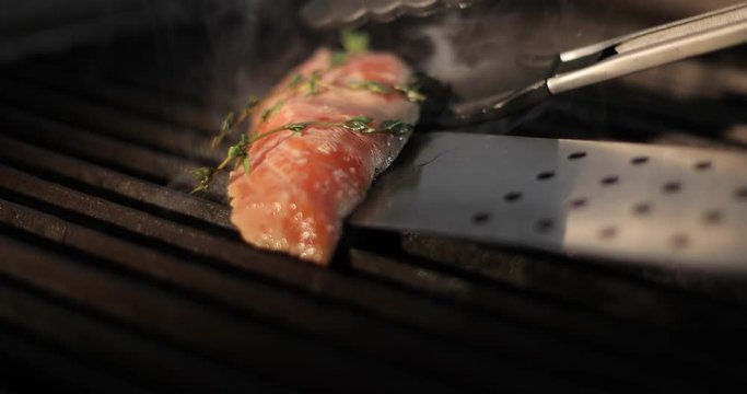 Cook flips a piece of fresh red fish sirloin on an electric grill using metal tongs.