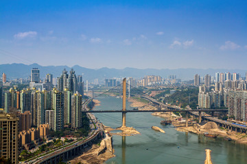 Obraz premium Chongqing, Chiny - 20 marca 2018: Widok z góry rzeki Jialing w chińskim mieście Chongqing. Mosty, drogi, bloki miejskie, góry. Słoneczny dzień.