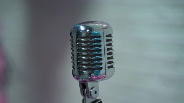 Silver vintage glare microphone on stage in retro club close up. Light shine on a beautiful chrome retro mic on scene against on white blurred background.