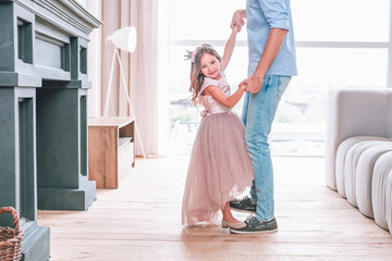 small girl standing on fathers shoes while dancing together at home