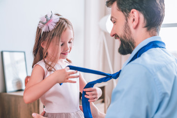 cute daughter helping daddy with tie before going for a work