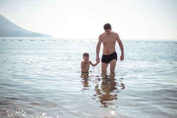 Young father and his little son play together in a water. Scenic sea and mountain view, summer time vacation