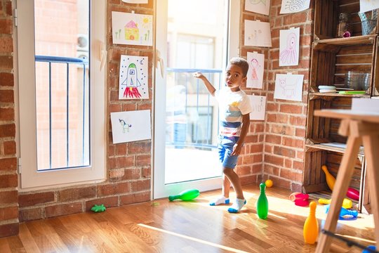 Beautiful african american toddler standing pointing with finger to the window at kindergarten