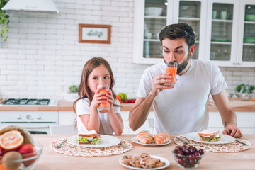 cute girl with her father drinking juice for breakfast on the kitchen together