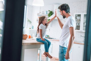 happy father and girl giving high five together on the kitchen