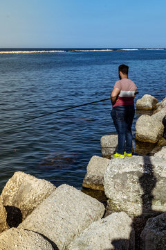 Joven pescando en el mar parado sobre las rocas 
