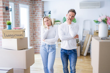 Fototapeta na wymiar Young beautiful couple standing at new home around cardboard boxes thinking looking tired and bored with depression problems with crossed arms.