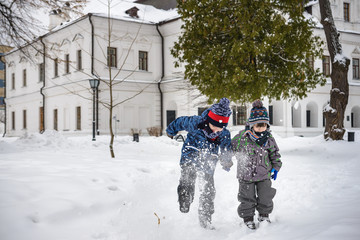 Two little kid boys in colorful clothes, outdoors during snowfall. Active outdoors leisure with children in winter on cold snowy days. Happy siblings having fun with snow. Travel in winter city