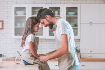 daughter sitting on the table and dad standing on the kitchen and looking at each other, side view