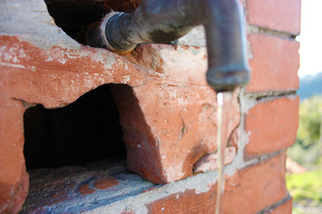 a rusty and old drinking water tap and an old red brick wall. drop of falling water pushed down by gravity