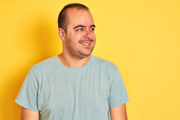 Obraz premium Young man wearing green casual t-shirt standing over isolated yellow background looking away to side with smile on face, natural expression. Laughing confident.