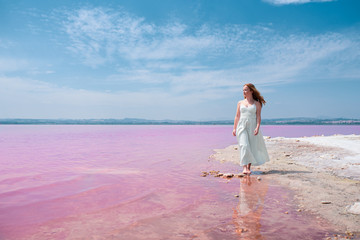 cute teenager woman wearing white dress walking on a amazing pink lake