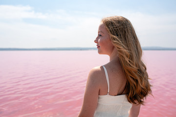Fototapeta na wymiar Side view of cute teenager woman wearing summer clothes standing on an amazing pink lake