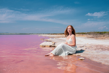 Fototapeta na wymiar cute teenager woman wearing white dress sitting on an amazing pink lake