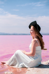 Fototapeta na wymiar cute teenager woman wearing white dress sitting on an amazing pink lake