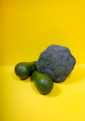 Two green avacados and broccoli on a yellow background