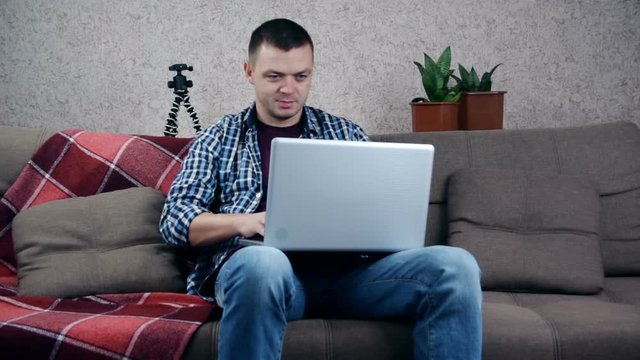 Attractive man sitting on the sofa using laptop at home on living background for chatting with friends. Indoor.