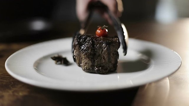Cooks hand puts a fresh fried steak on white plate and maiking final decoration of dish.