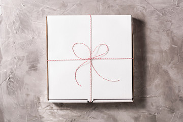 Closed box of pizza tied of christmas red white string or twine in a bow on the on grey concrete background. Concept