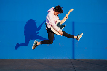 young man jumping with electric guitar on blue background