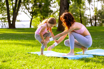 young woman teaching little girl yoga in the park