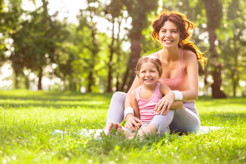 Naklejka na ściany i meble mother and daughter sitting in the park together and smiling at the camera