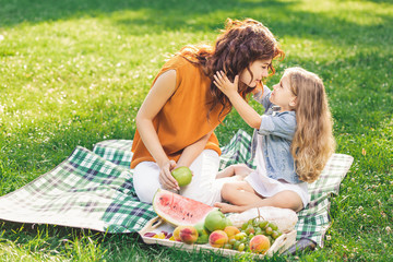 adorable girl hugging her mother in the park sitting on the blanket