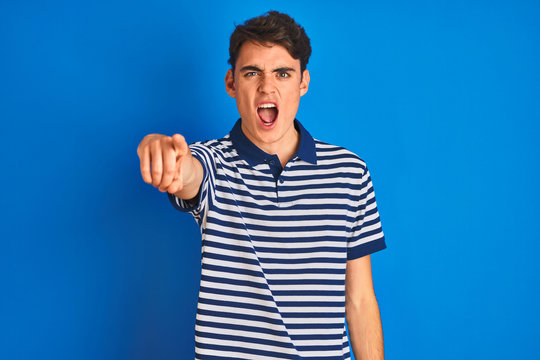 Teenager boy wearing casual t-shirt standing over blue isolated background pointing displeased and frustrated to the camera, angry and furious with you