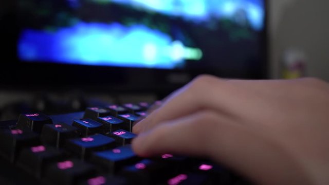 Closeup of male hand using illuminated PC gaming keyboard. Gamer is unpausing game and continues his playthrough. Danger of gaming addiction for young generation.