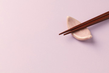 Wooden chopsticks and chopstick rest on bright paper background. Close up. Copy space. 