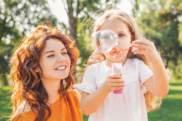 portrait of girl blowing soap bubbles in the park with mother