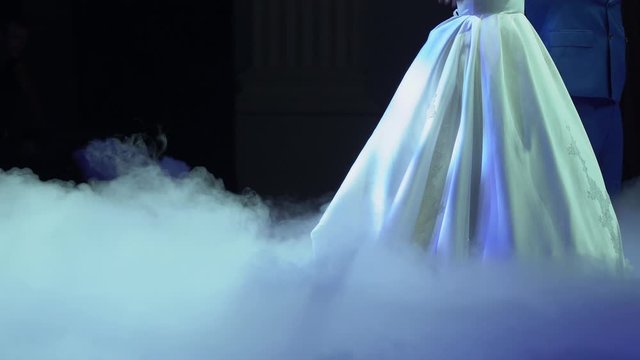 First dance of wonderful loving couple in happy married day. Handsome man - groom hold beautiful elegant bride in white wedding dress in thick puffs of blue fluffy smoke on the floor close up.