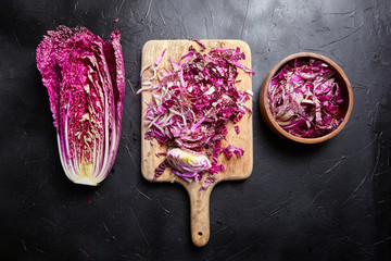 Chopped Red Chinese cabbage (Purple wombok) on wooden cutting board and bowl on stone table. Half...
