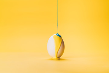 Color paint slow flowing on white egg howering in air at yellow background, colored liquid mixing...