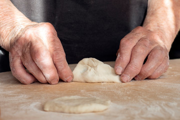 The hands of an old woman are making pies out of dough.